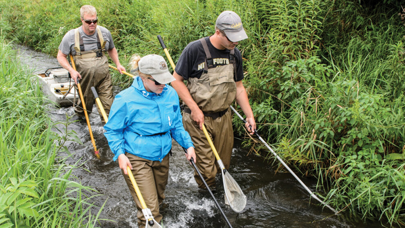 three people walking in a stream.