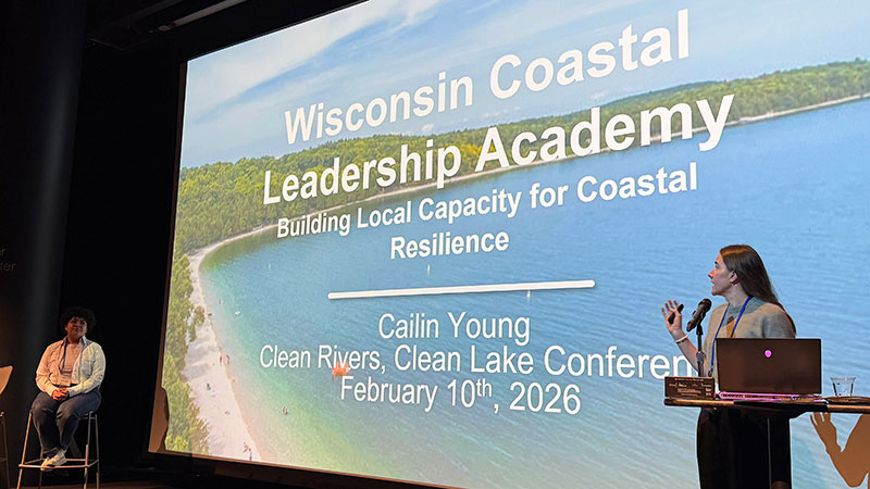 Presenter at a podium standing in front of a large screen.